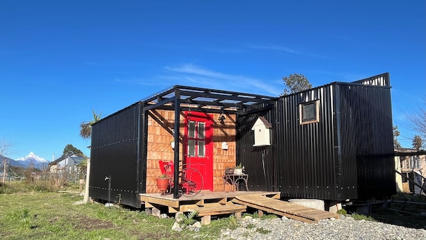 Une petite cabane en bois avec une porte rouge, un revêtement extérieur noir et une terrasse en bois.