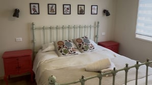 Une chambre à coucher avec un lit en métal, une table de chevet rouge, une commode rouge et une fenêtre avec des stores.