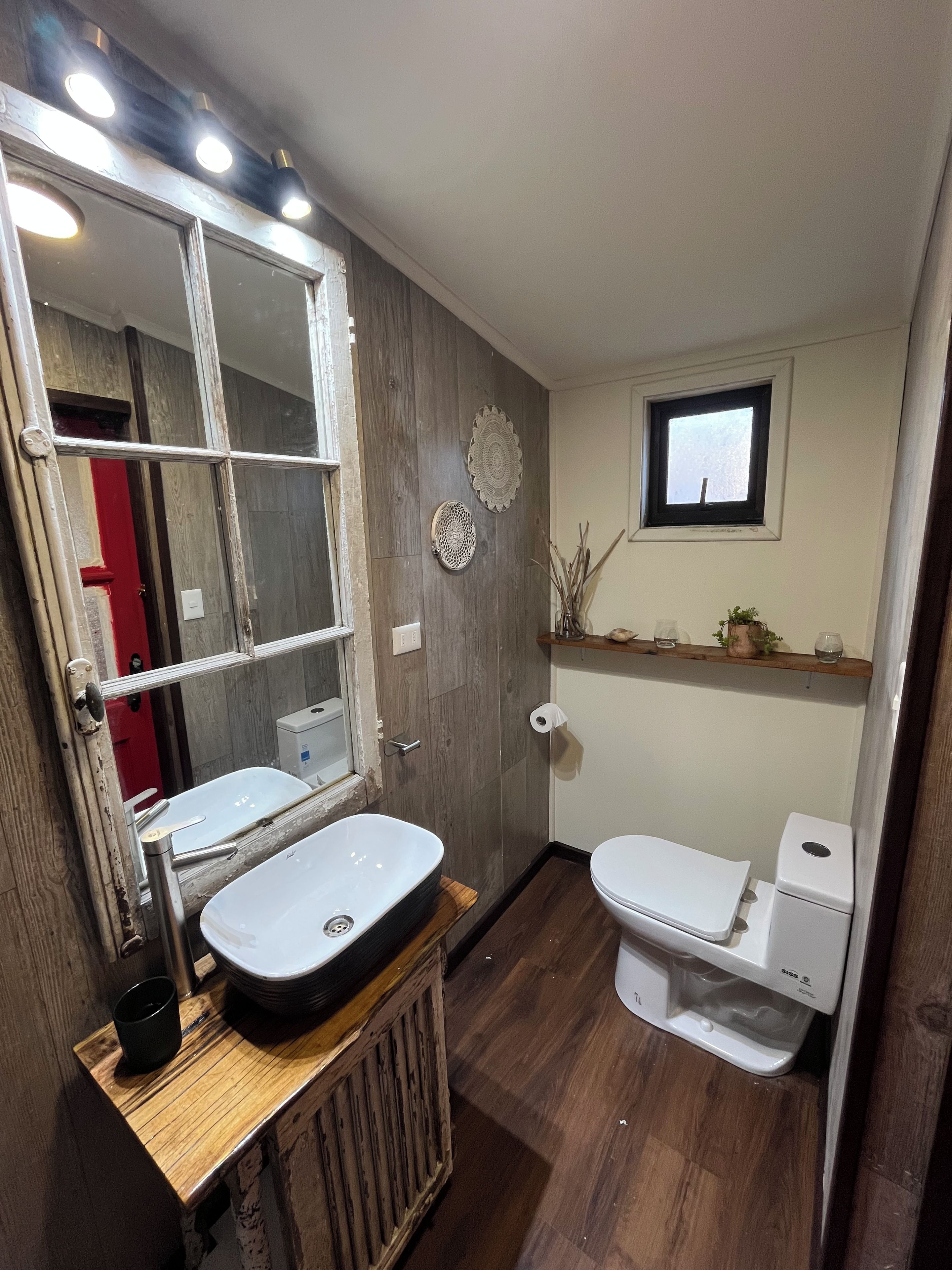 Un baño con tocador de madera, lavamanos, inodoro y espejo con luces.