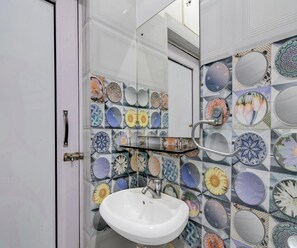 A bathroom with a white sink, a mirror, and a wall decorated with various circular tiles. - Classic Raj Guest House (Barakpur)