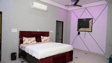 Un dormitorio con cama, ventilador de techo, unidad de aire acondicionado, televisor montado en la pared y una puerta.