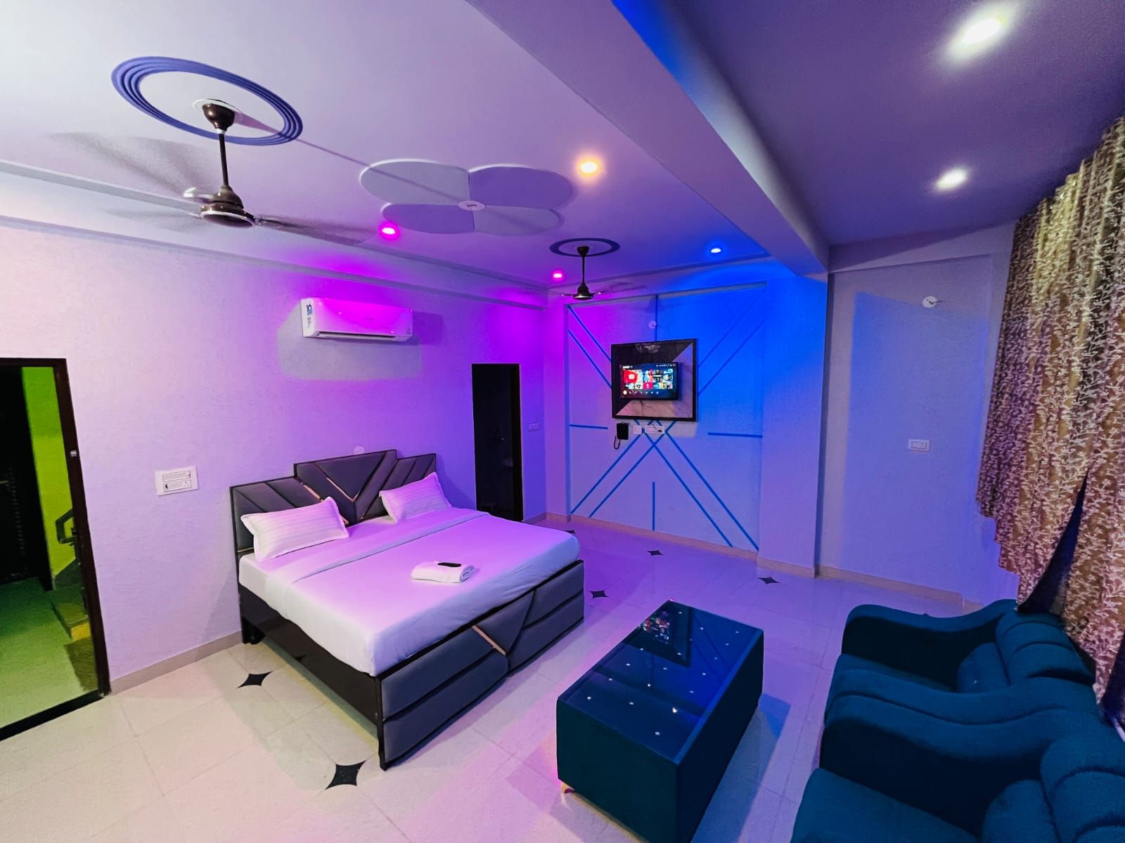 A modern bedroom with a bed, a TV on a stand, a ceiling fan, and a wall-mounted air conditioner.
