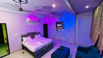 A modern bedroom with a bed, a TV on a stand, a ceiling fan, and a wall-mounted air conditioner.