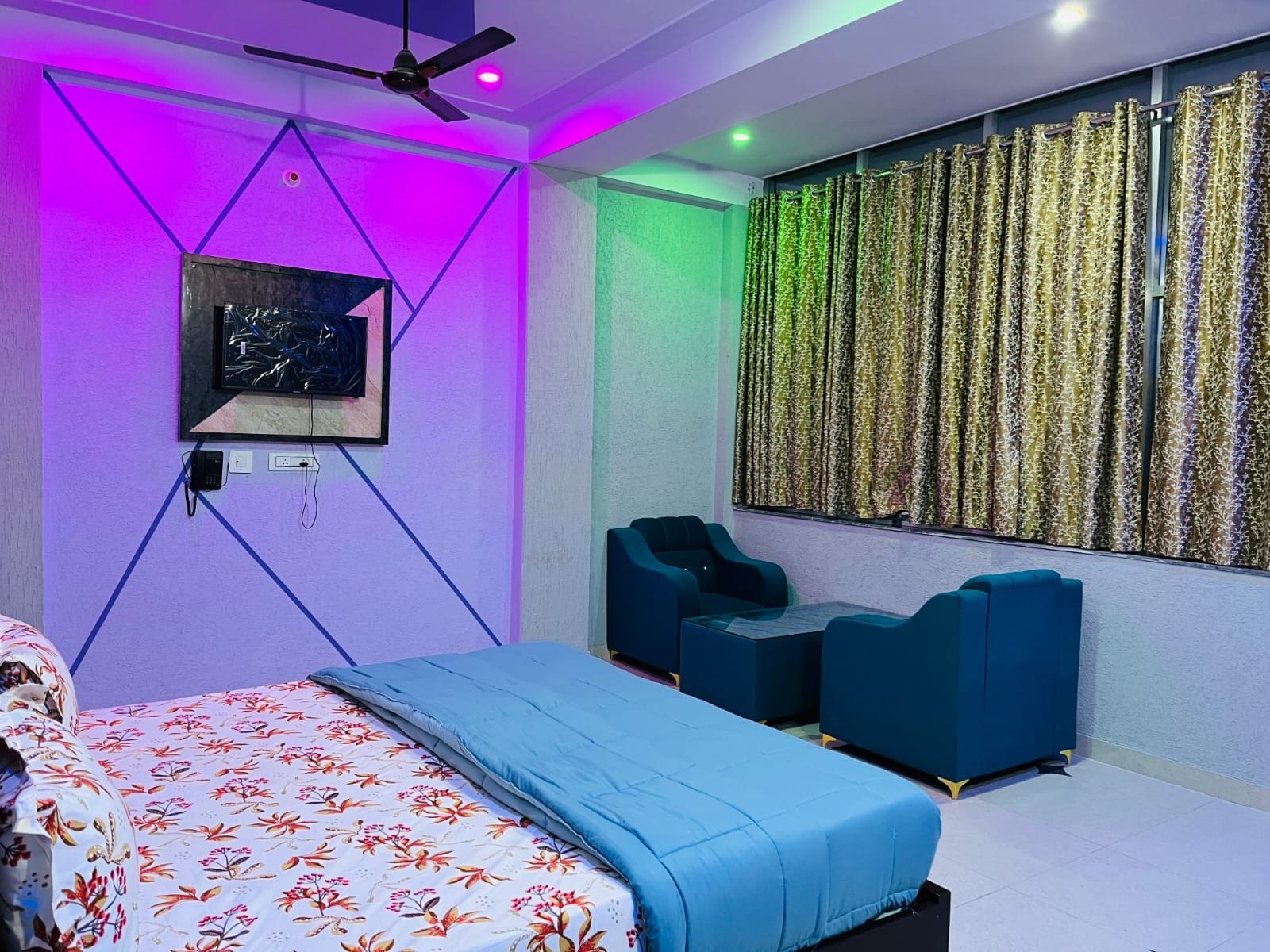 A modern bedroom with a bed, two seating areas, a ceiling fan, and a wall-mounted TV.