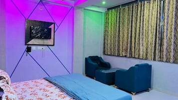 A modern bedroom with a bed, two seating areas, a ceiling fan, and a wall-mounted TV.