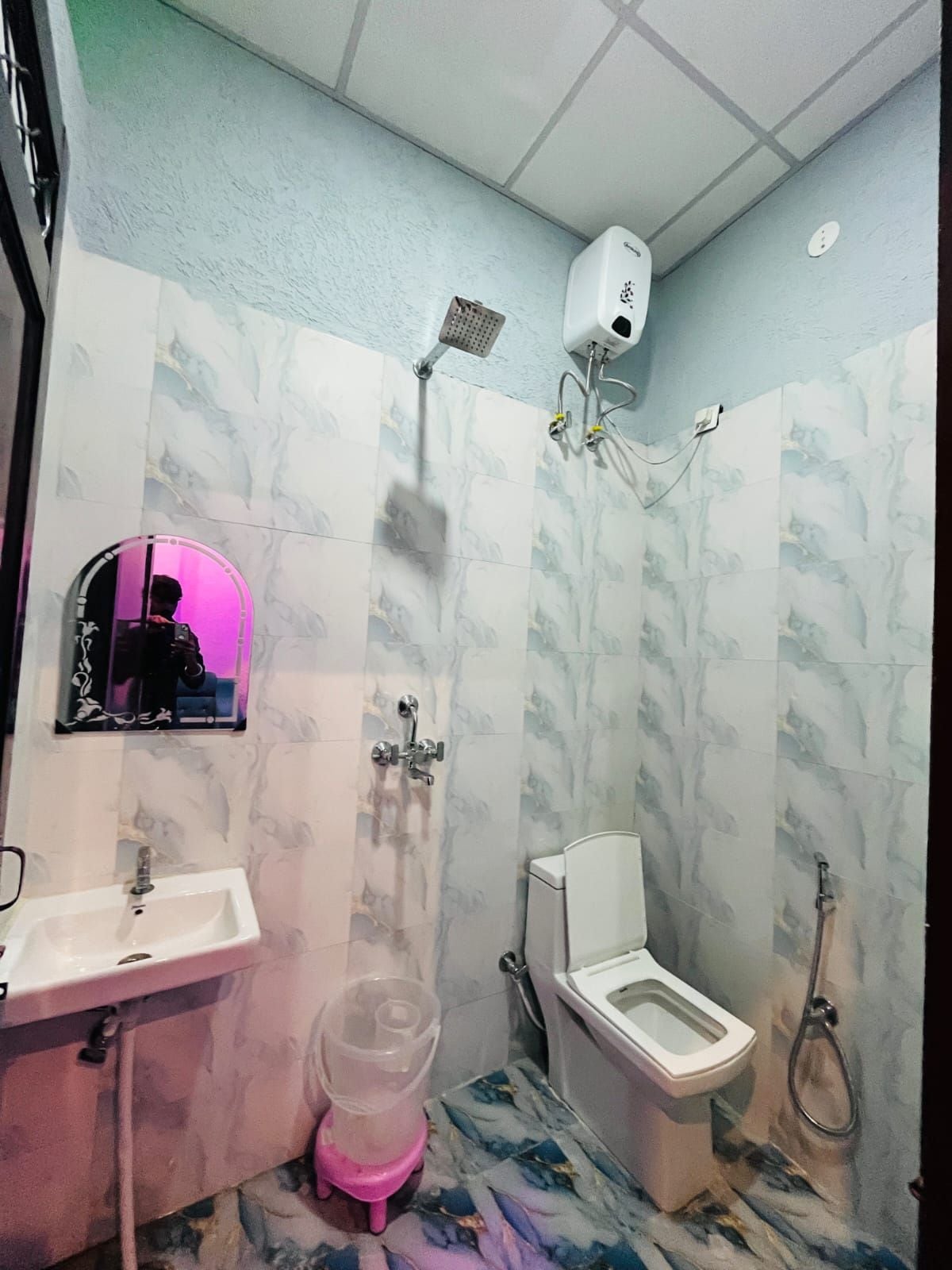 Un baño con ducha, inodoro, lavamanos y un espejo con luz rosa.