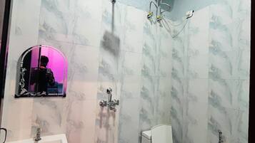 Un baño con ducha, inodoro, lavamanos y un espejo con luz rosa.