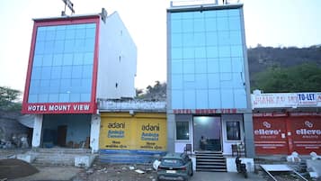 A hotel named 'Hotel Mount View' with a red and white facade, a yellow signboard for 'Adani Ambuja Cement,' and a 'To-Let' signboard.