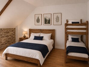 Un dormitorio con una cama de madera, literas y una pared de piedra. Hay tres cuadros en la pared.