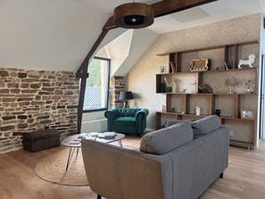 Un salón tipo loft con pared de piedra, un sillón verde, un sofá gris y una estantería de madera.