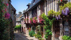 A cobblestone street lined with traditional half-timbered houses, each adorned with flowering plants and potted greenery. - Vrbo Property (Locmaria-Grand-Champ)