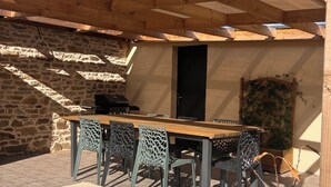 An outdoor patio with a wooden pergola, a stone wall, and a table with chairs. - Vrbo Property (Locmaria-Grand-Champ)