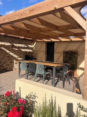 An outdoor patio with a wooden pergola, a stone wall, and a table with chairs. - Vrbo Property (Locmaria-Grand-Champ)