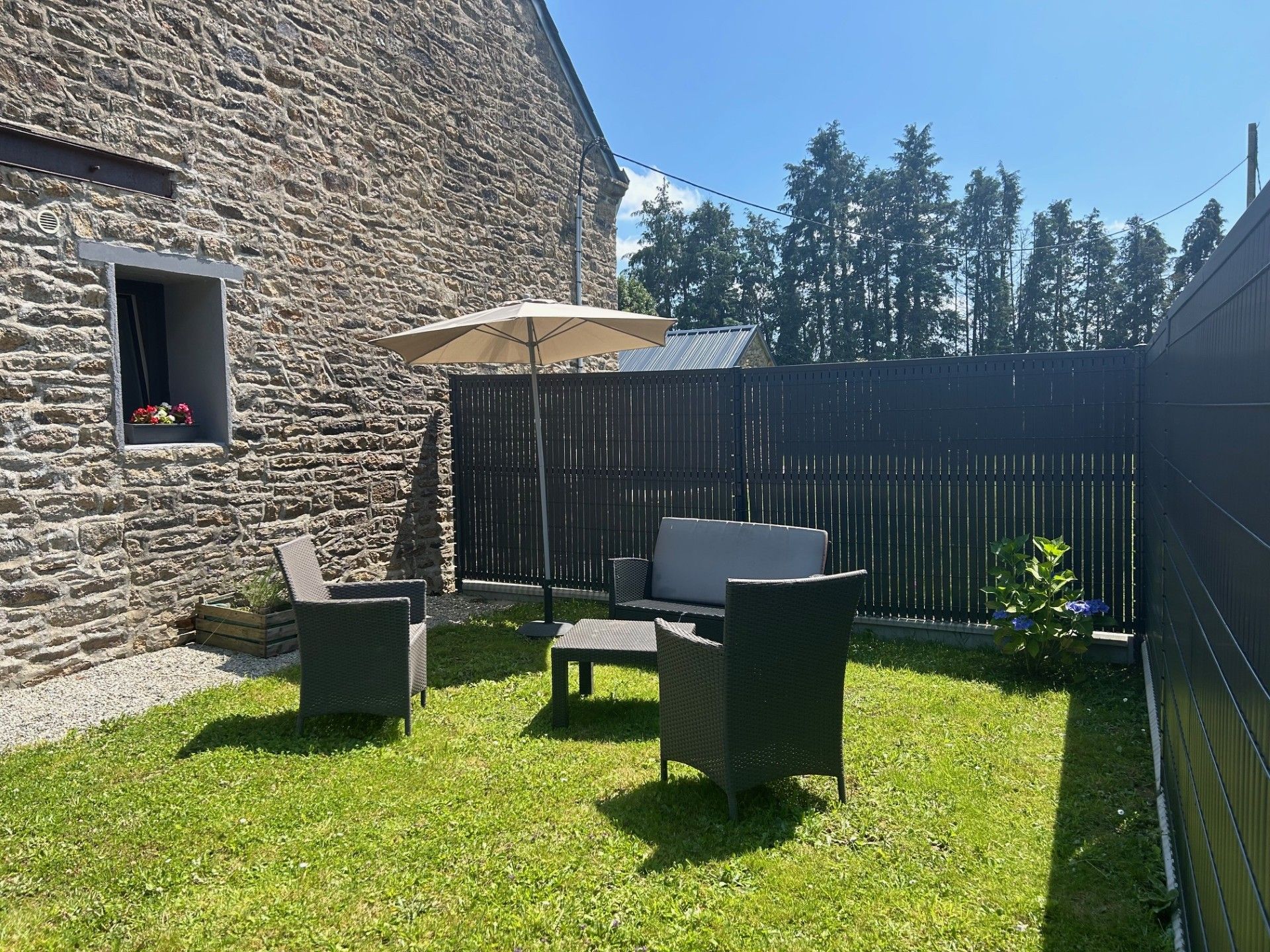 Ein Steinhaus mit einem Fenster, einer Terrasse mit Korbmöbeln und einem Holzzaun.