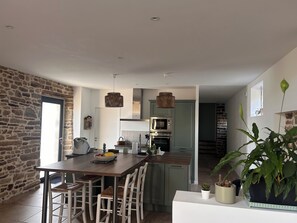 Une cuisine moderne avec un mur en pierre, une table à manger en bois, des chaises blanches et une plante en pot.
