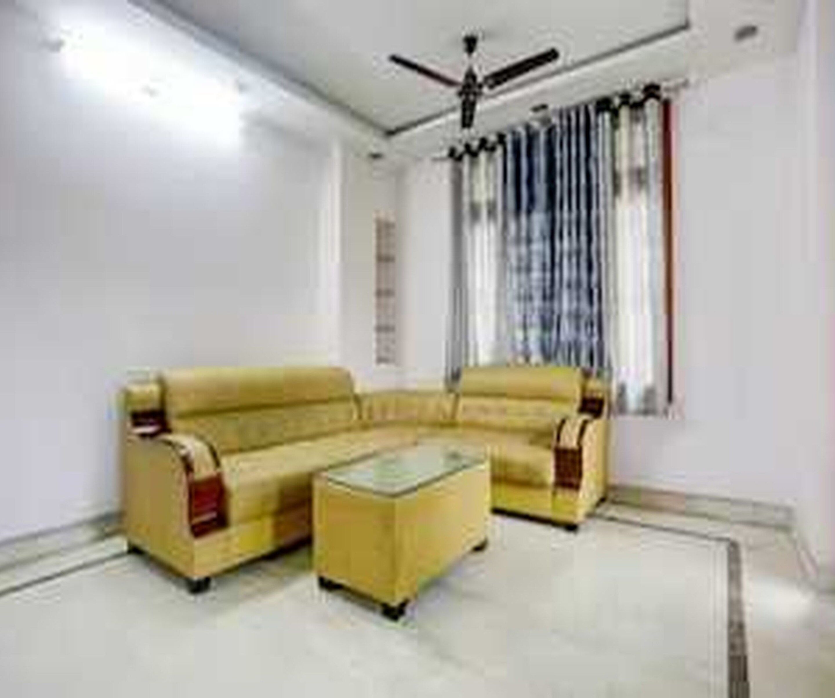 A living room with a yellow sofa set, a glass coffee table, and a ceiling fan.