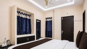 Quarto de hotel com cama, escrivaninha, espelho, guarda-roupa e porta.