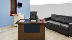 Quarto com escrivaninha, sofá de couro preto, pequeno armário e televisão na parede.