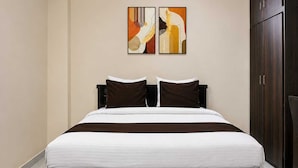 Quarto de hotel com cama grande, cabeceira de madeira escura, duas pinturas penduradas na parede e um guarda-roupa.