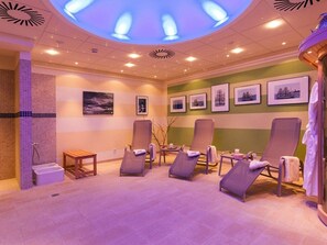 Ein Spa-Raum mit Liegesesseln, einer Massageliege und Kunstwerken an den Wänden.