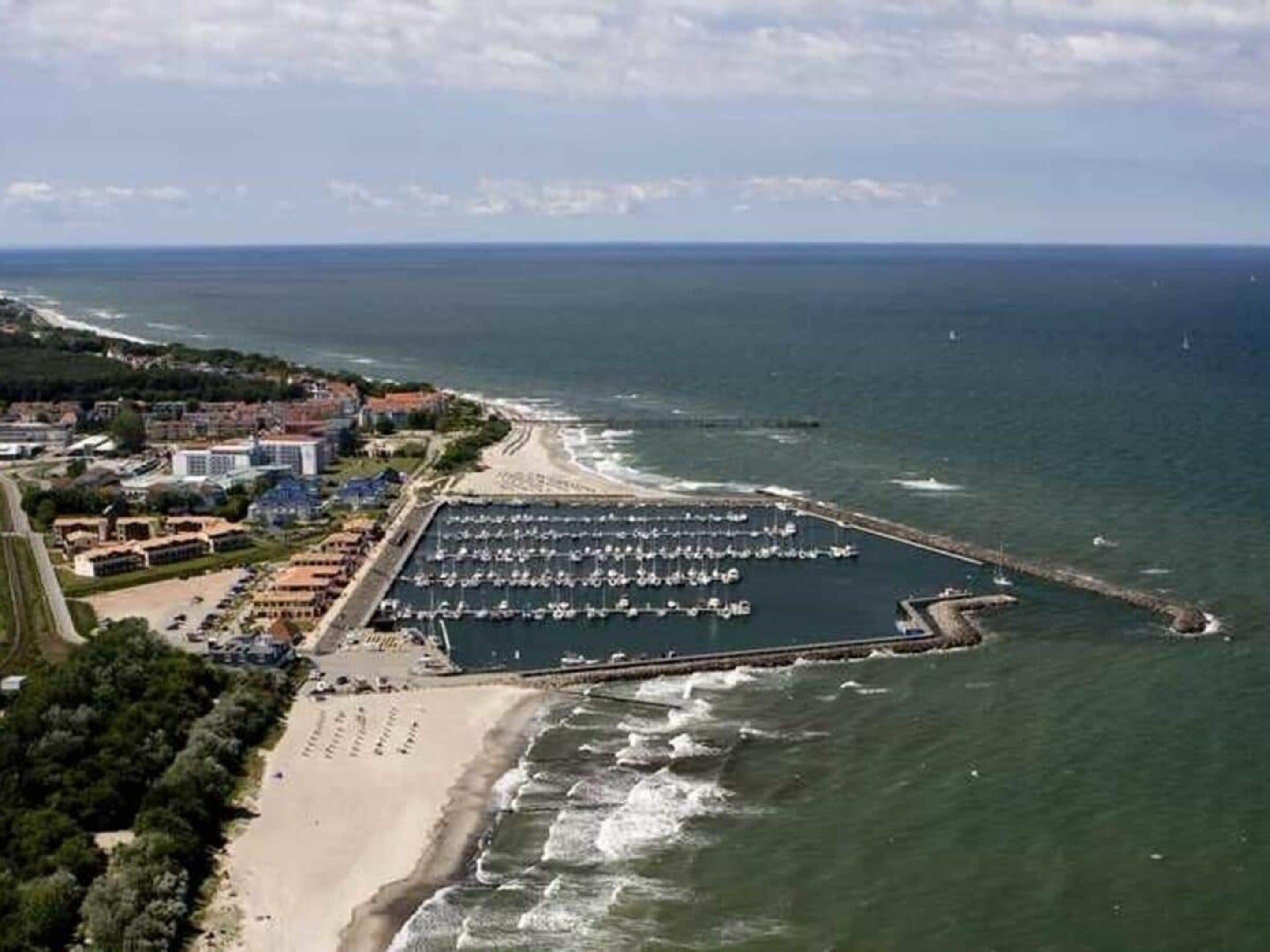 An aerial view of a coastal area with a marina, beach, and adjacent buildings.