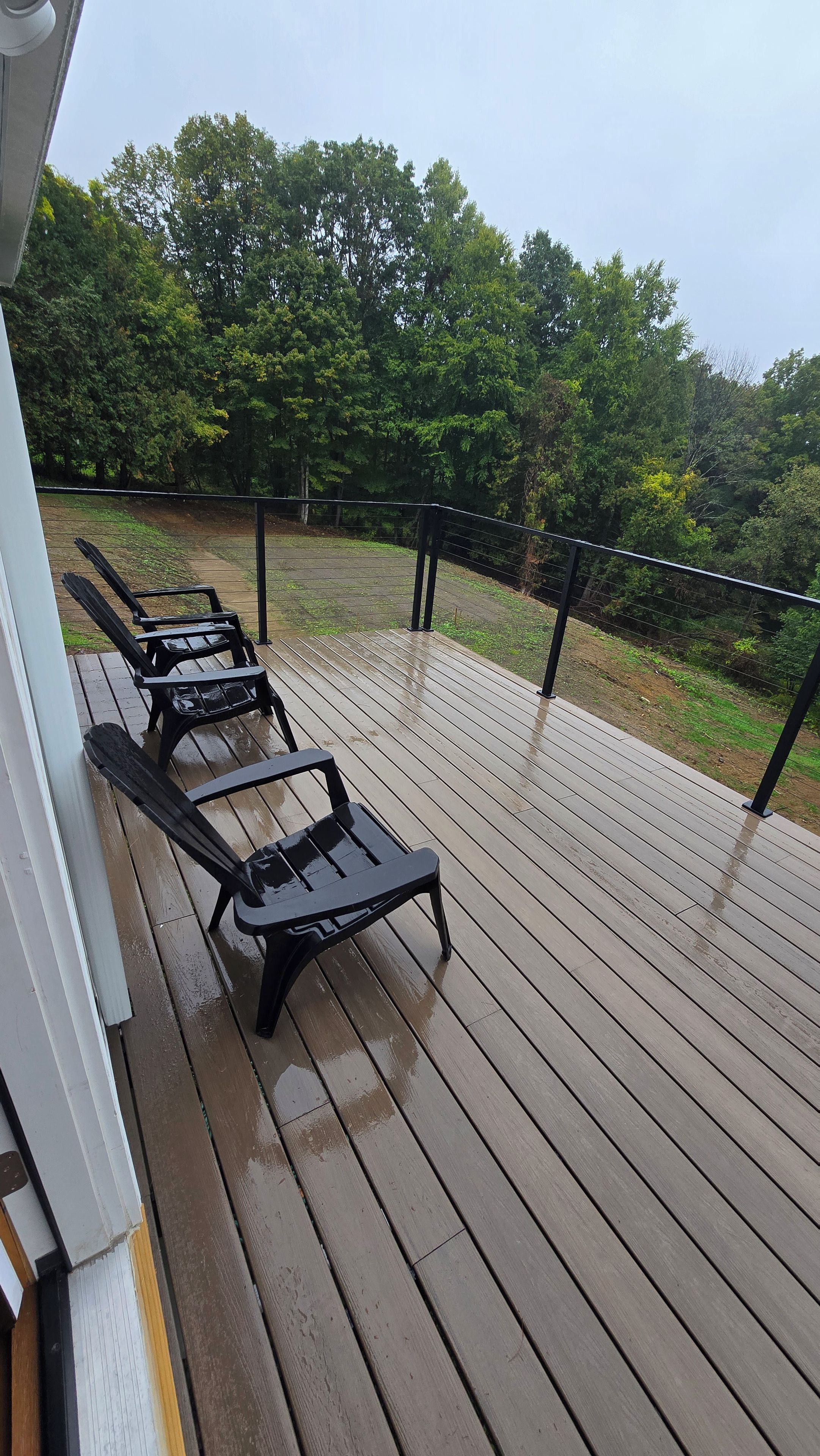 Een houten terras met vier zwarte lounge stoelen.