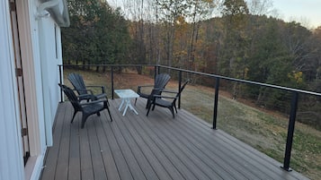 Eine Holzterrasse mit zwei Adirondack-Stühlen und einem kleinen Tisch, mit Blick auf eine bewaldete Landschaft.