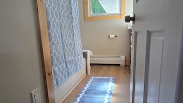 Un pasillo con suelo de madera, una cortina azul estampada, un ventanal con vistas a follaje, y una puerta blanca.