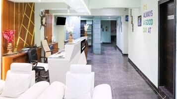 A hotel lobby with a reception desk, seating area with white sofas, a clock, and a sign on the wall.