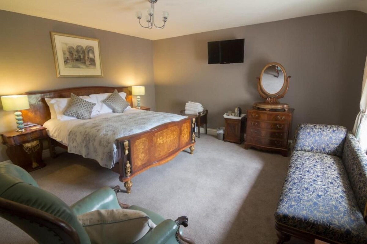 A bedroom with a large bed, a dresser, a chair, a television, and a painting on the wall.