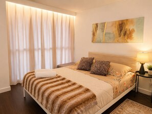 Ein Hotelzimmer mit Bett, Nachttisch, Lampe, einem Bild und einem Fenster mit Vorhängen.