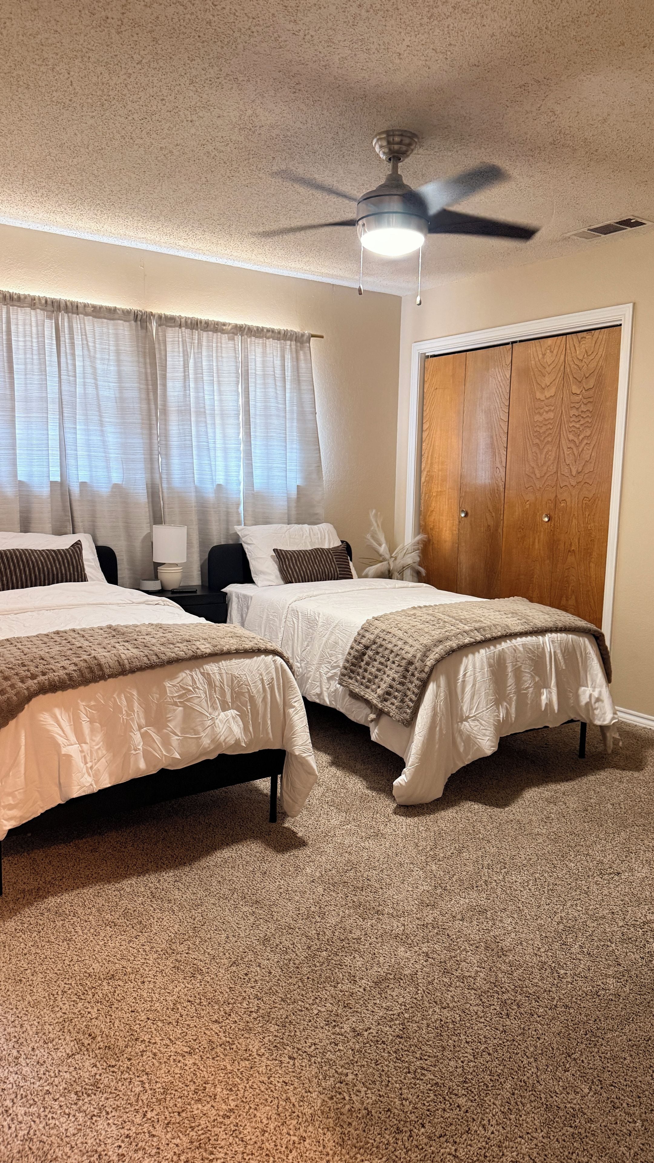 Ein Schlafzimmer mit zwei Betten, einem Deckenventilator, einem Holzschrank und einem Teppichboden.