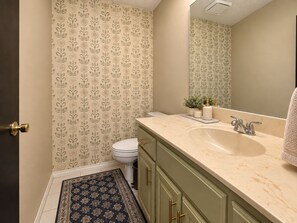 Une salle de bain avec des toilettes, un lavabo, un miroir et un papier peint à motifs.
