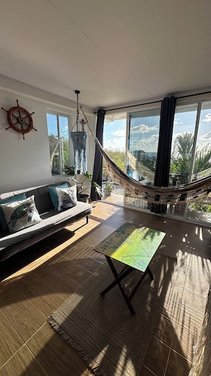 Ein Wohnzimmer mit einer Hängematte, einer Couch mit Kissen und Blick ins Freie.