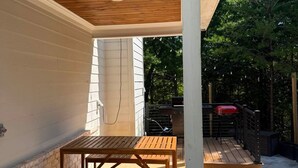 Un patio al aire libre con una mesa y sillas de madera, un área cubierta con techo blanco y una pared de ladrillo.