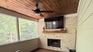 Un área de estar al aire libre acogedora con mobiliario de mimbre, un televisor de pantalla plana y una chimenea.