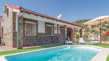 A house with a swimming pool, stone walls, and a red-tiled roof.