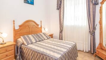 A bedroom with a wooden bed, bedside tables, a mirror, curtains, and a wall-mounted picture.