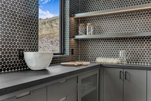 A modern kitchen with a black and white tiled backsplash, a large white bowl, and a wooden cutting board on the counter. - Wasatch View - Luxury Alpine Retreat with Private Hot Tub and Mountain Views (Daniel)