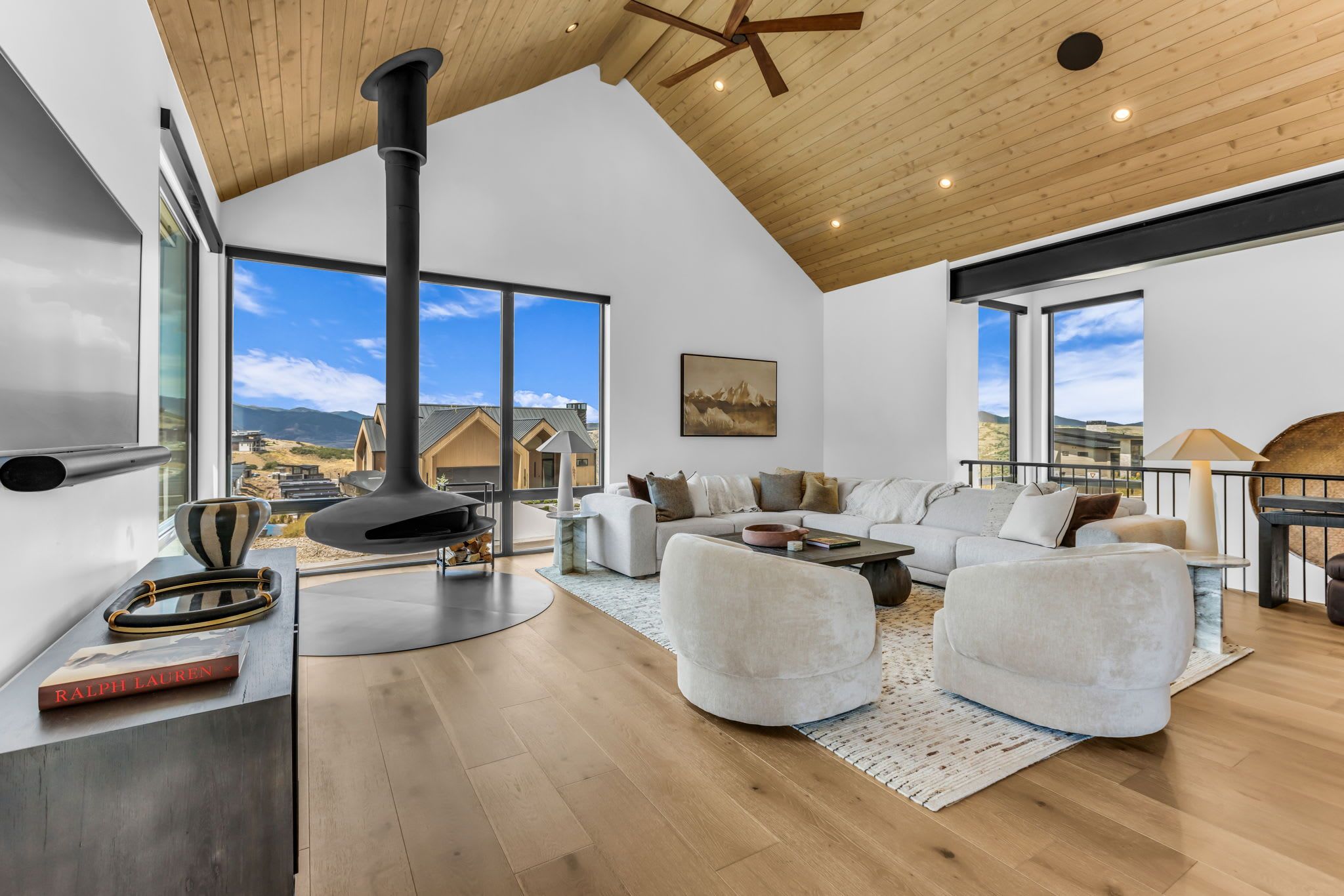 A spacious living room with a large fireplace, a sofa set, and a view of the surrounding landscape.