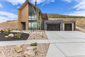A modern two-story house with a garage, a landscaped front yard with rocks and plants, and a clear sky. - Wasatch View - Luxury Alpine Retreat with Private Hot Tub and Mountain Views (Daniel)
