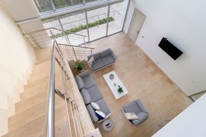 Un salon moderne avec un escalier, un ensemble de canapés, une table basse et un téléviseur fixé au mur.