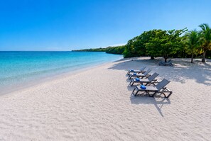 A beach with clear turquoise water, white sand, and several sun loungers with blue cushions. - Modern Luxury Villa with Resort Pool  Bright Open Spaces Near Cartagena Beaches (Bolívar)