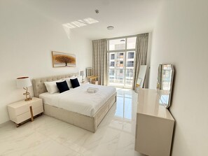 Une chambre d’hôtel moderne avec un grand lit, une table de chevet avec une lampe, une coiffeuse avec un miroir et une vue sur la ville par la fenêtre.