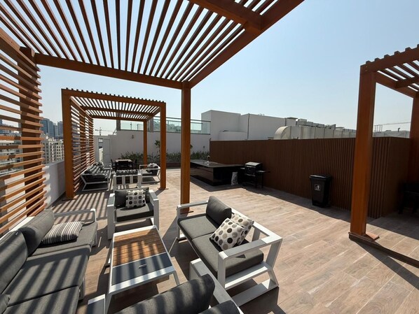 Un espace extérieur aménagé en terrasse, doté de pergolas en bois, de plusieurs coins salon et d’un barbecue.