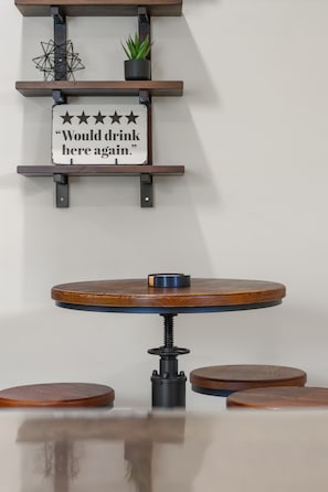 Una mesa redonda con un pilar central, rodeada por cuatro taburetes. Encima de la mesa hay dos repisas con objetos decorativos y un letrero.
