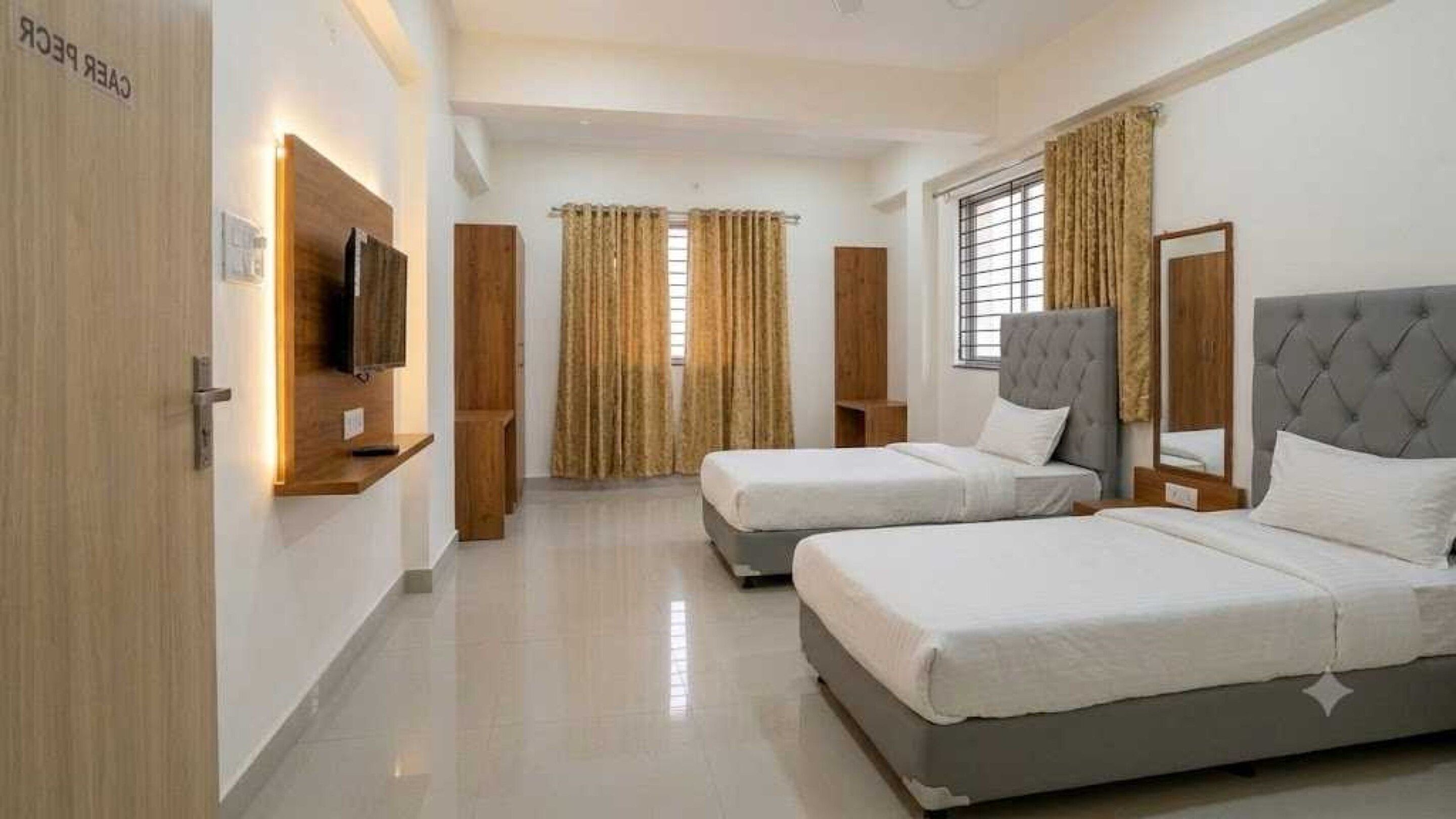 A hotel room with two beds, a television, and a window with curtains.