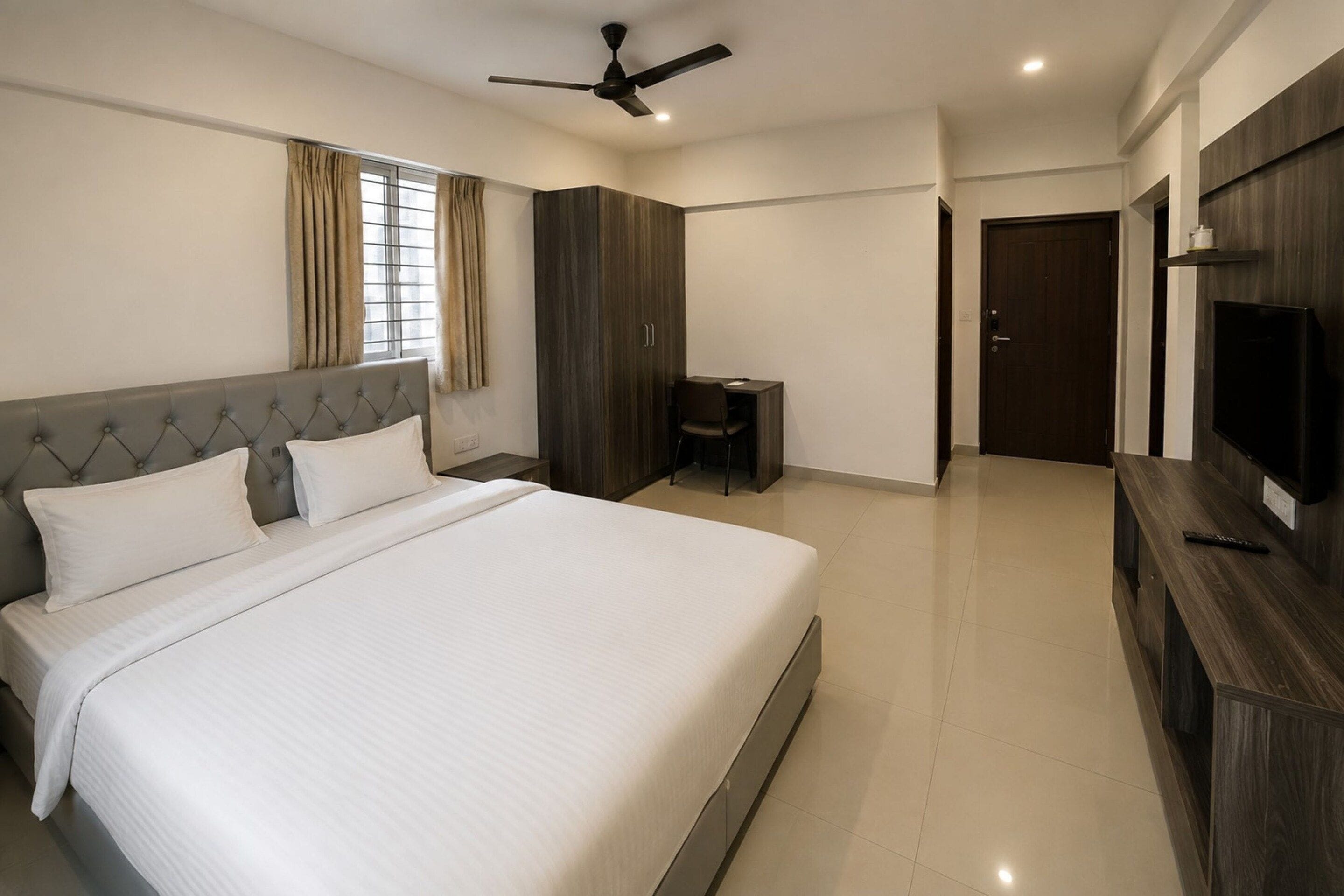 Habitación de hotel con una cama grande, un escritorio, una silla, un armario, un televisor y un ventilador de techo.