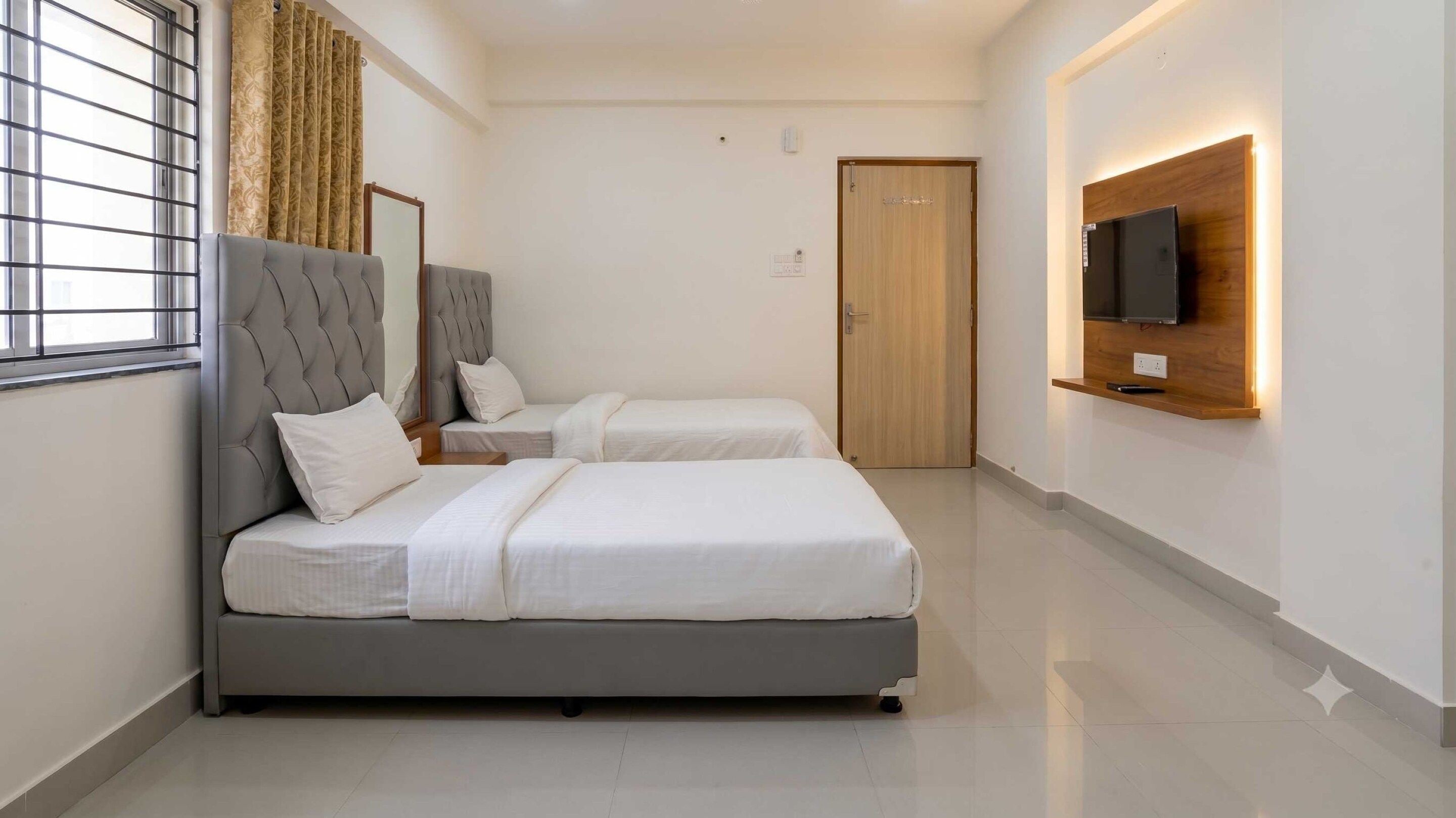 A hotel room with two beds, a television mounted on the wall, and a window with curtains.