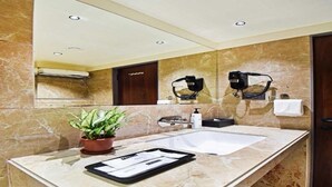 A bathroom with a large mirror, a sink, a potted plant, and two hair dryers mounted on the wall. - Deluxe Hotel Urban Oasis (Pune)